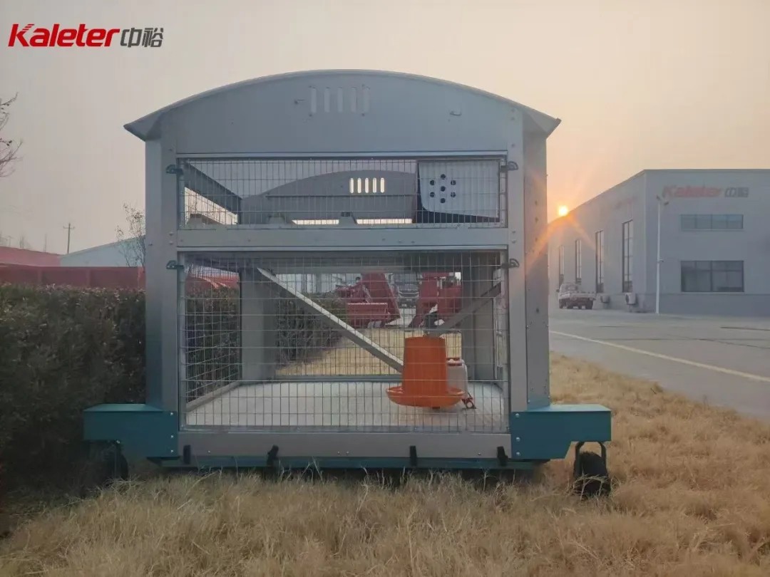 Kaleter small family mobile chicken house on grass at dusk, with the Kaleter facility in the background