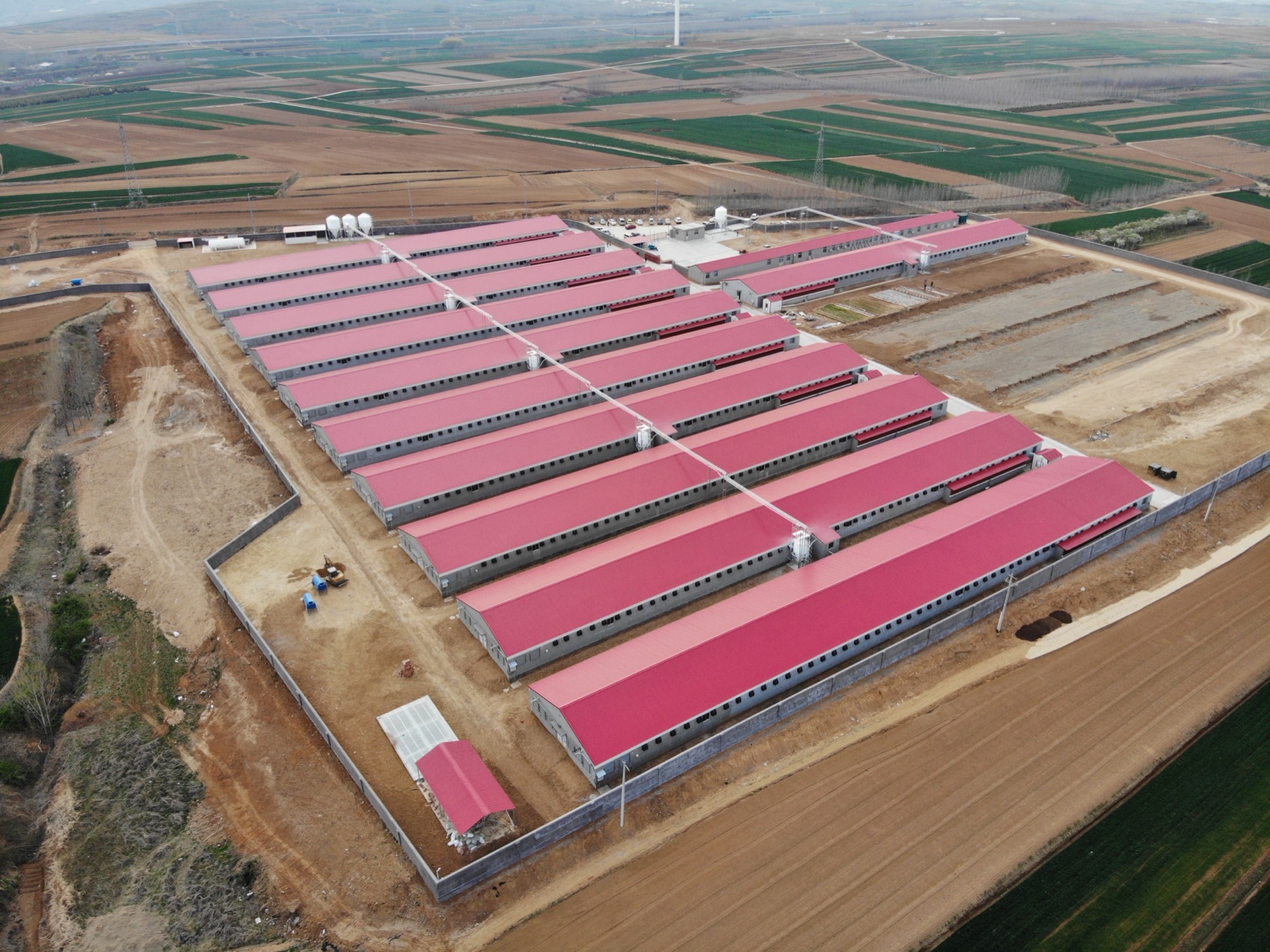 A large breeder complex with red-roofed houses, with site work still underway alongside
