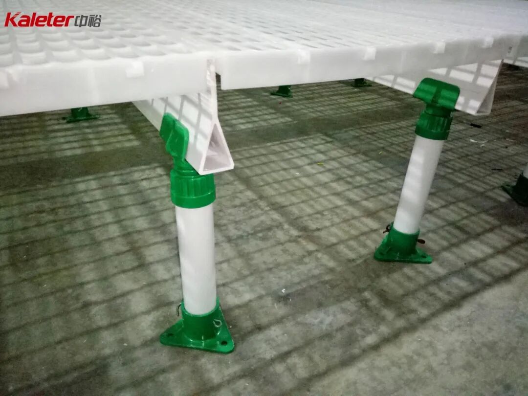 A close view under the slat panel showing two adjustable white support legs with green fittings resting on a concrete floor