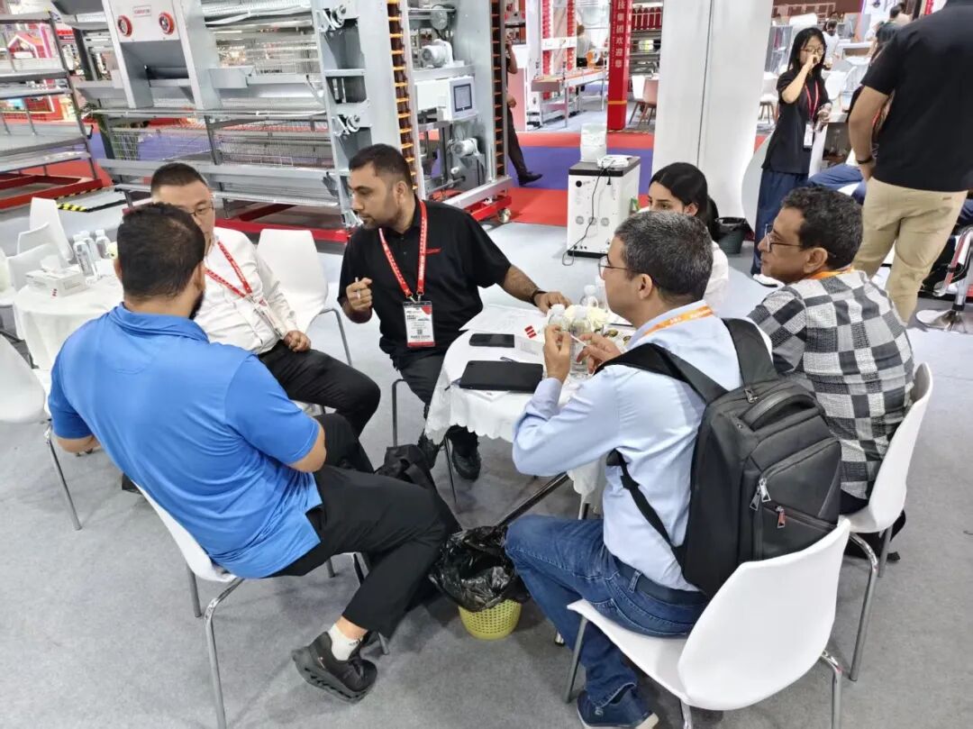 Visitors seated with Kaleter staff at the booth, talking beside a layer cage display